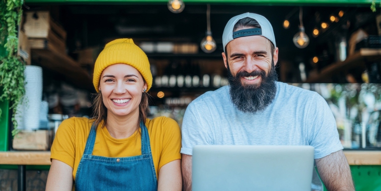 Two people working together on a laptop outside a small business.