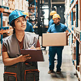 Two men and a woman in hard hats working in a warehouse